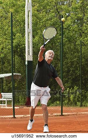 Stock Image - Senior male tennis player serving. Fotosearch