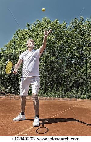Stock Image - Senior tennis player serving. Fotosearch