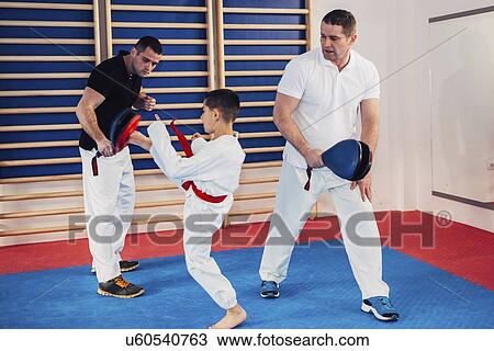 Stock Image - Taekwondo instructors working with boy. Fotosearch