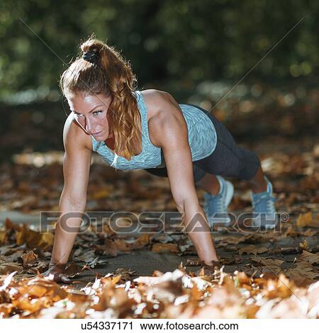 Stock Image - Woman doing push ups in the park. Fotosearch