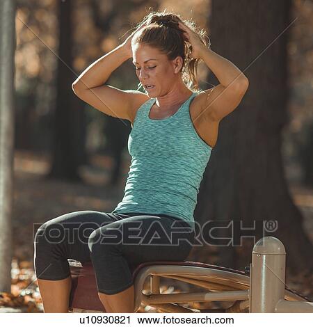 Stock Image - Woman doing sit ups in the park. Fotosearch