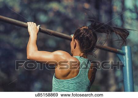 Stock Photo - Woman exercising on horizontal bar outdoors. Fotosearch