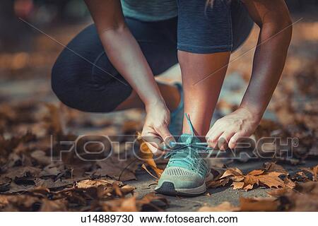 Stock Image - Woman kneeling and tying shoe. Fotosearch