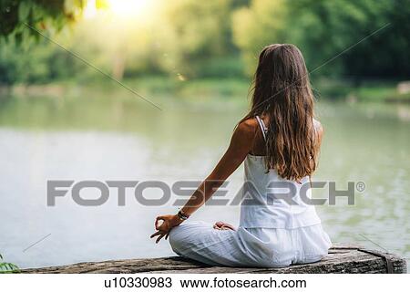 Stock Image - Woman meditating by a lake. Fotosearch