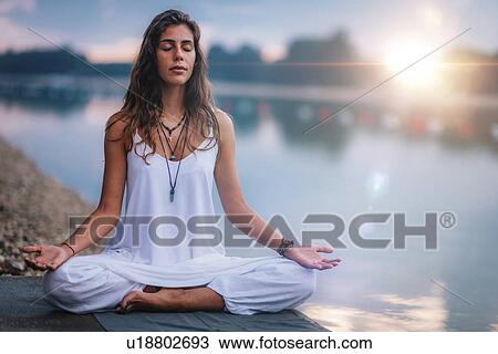 Stock Image - Woman meditating by a lake. Fotosearch
