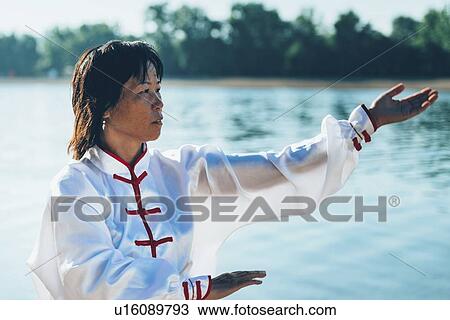 Stock Image - Women practicing tai chi by lake. Fotosearch