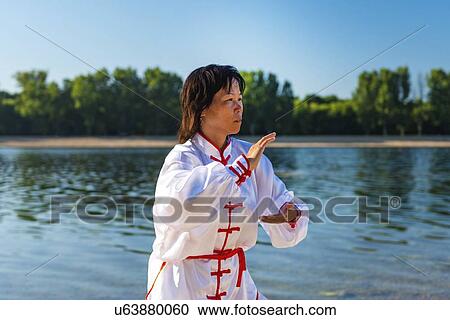 Stock Image - Women practicing tai chi by lake. Fotosearch