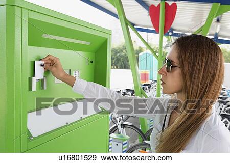 Stock Photo - Young woman using bicycle sharing system. Fotosearch