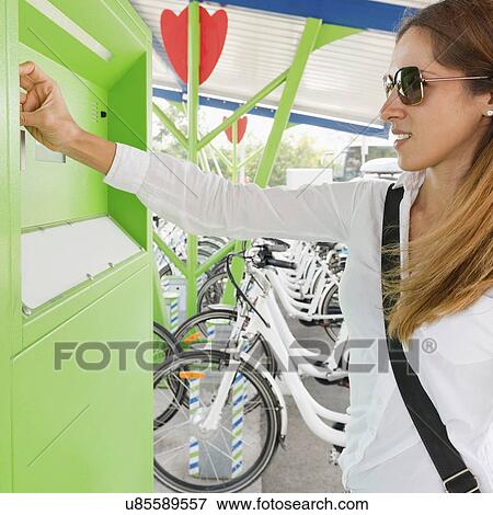 Stock Photo - Young woman using bicycle sharing system. Fotosearch