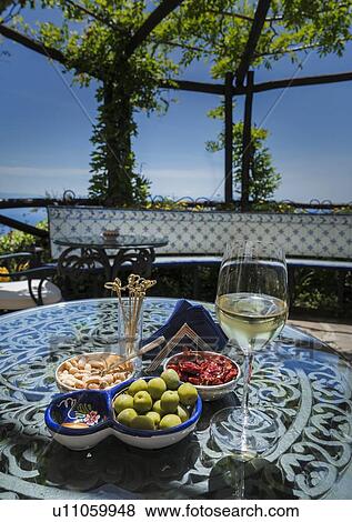 Stock Photo - Antipasto and wine on dining table under pergola. Fotosearch