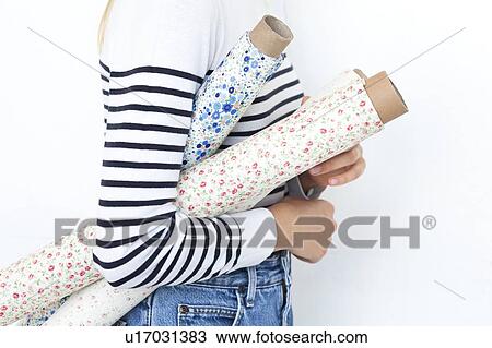 Stock Image - Arm of woman holding rolls of floral pattern fabric. Fotosearch