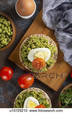Stock Image - Avocado with egg and tomato on rice cakes. Fotosearch