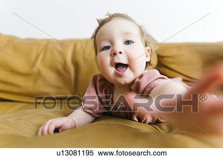 Stock Photography - Baby girl reaching for camera on sofa. Fotosearch