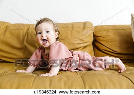 Picture - Baby girl wearing pink outfit on sofa. Fotosearch