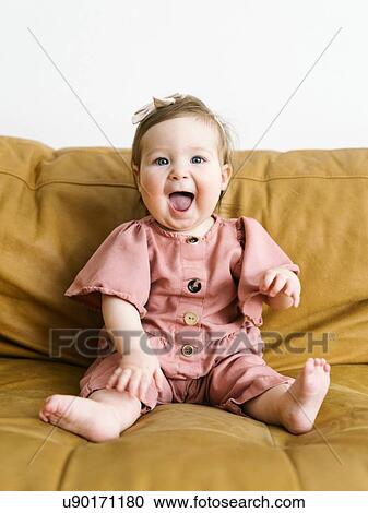 Stock Image - Baby girl wearing pink outfit on sofa. Fotosearch