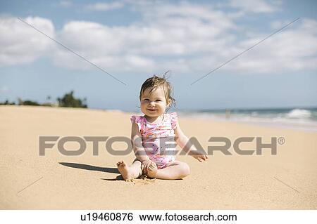 Stock Photograph - Baby girl wearing pink swimwear sitting on beach. Fotosearch