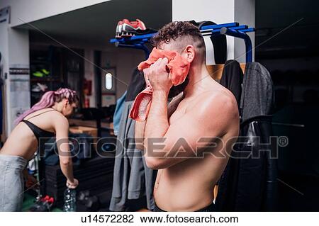 Stock Image - Bare chested young man training, drying face with towel in gym. Fotosearch