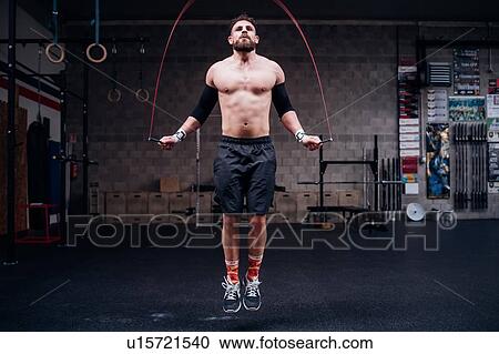 Stock Image - Bare chested young man training, skipping in gym. Fotosearch