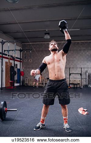 Stock Photograph - Bare chested young man training, lifting dumbbell in gym. Fotosearch