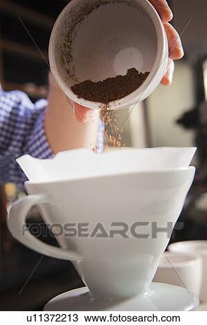 Stock Image - Barista pouring coffee grounds into filter. Fotosearch