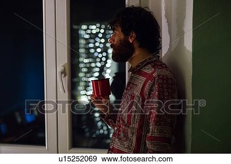 Stock Photo - Bearded young man in deep thought by window. Fotosearch