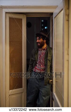 Stock Image - Bearded young man leaning against door. Fotosearch