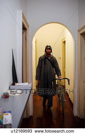 Stock Image - Bearded young man leaving home with bicycle. Fotosearch