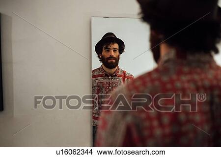 Picture - Bearded young man looking into mirror at home. Fotosearch