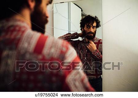 Picture - Bearded young man looking into mirror at home. Fotosearch