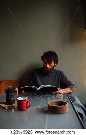 Stock Image - Bearded young man reading book at home. Fotosearch