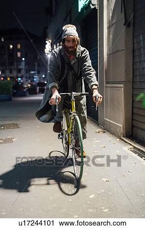 Stock Image - Bearded young man riding bicycle on pavement. Fotosearch
