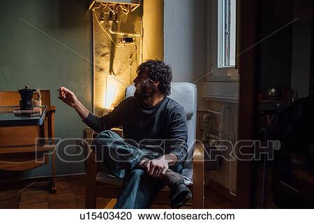 Stock Image - Bearded young man smoking at home. Fotosearch