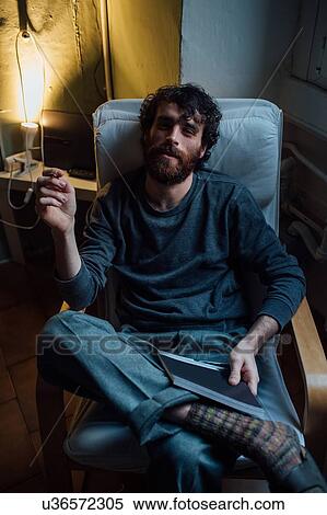 Stock Photography - Bearded young man smoking at home. Fotosearch