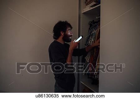 Stock Photography - Bearded young man talking on smartphone in front of wardrobe. Fotosearch