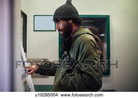 Picture - Bearded young man using cash machine. Fotosearch