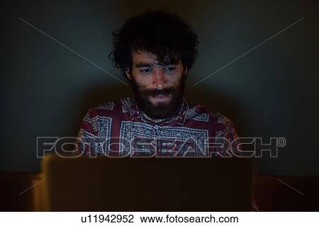 Stock Image - Bearded young man using laptop at home. Fotosearch