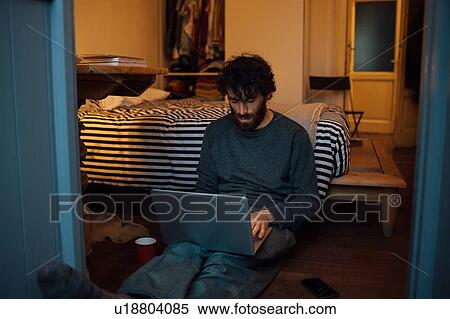 Stock Photography - Bearded young man using laptop in bedroom. Fotosearch