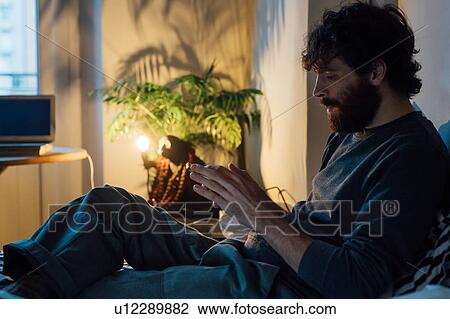 Stock Image - Bearded young man using smartphone in bed. Fotosearch