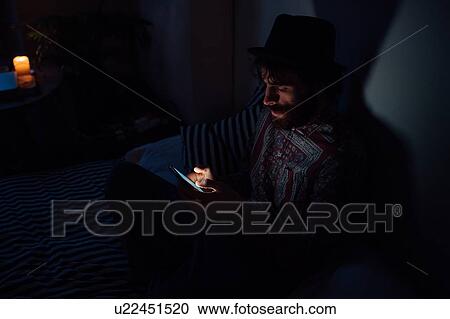 Bearded young man using smartphone in dark room View Large Photo Image Stock Image - Bearded young man using smartphone in dark room. Fotosearch