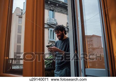 Bearded young man using smartphone on balcony View Large Photo Image Stock Image - Bearded young man using smartphone on balcony. Fotosearch