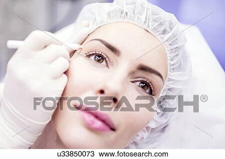 Stock Image - Beauty technician using pencil to mark woman's face for beauty treatment.. Fotosearch