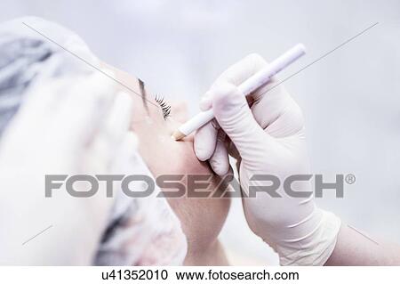 Stock Image - Beauty technician using pencil to mark woman's face for beauty treatment.. Fotosearch