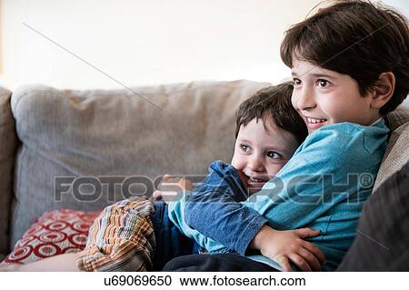 Stock Image - Big brother hugging toddler on sofa. Fotosearch