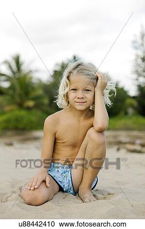 Stock Image - Blond haired boy kneeling on beach. Fotosearch