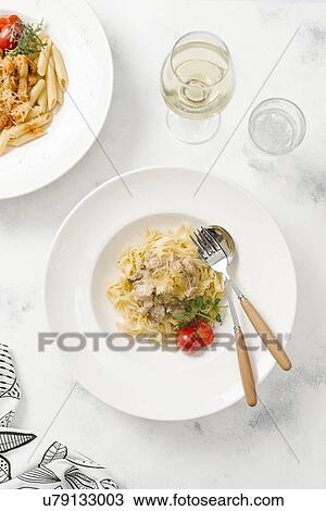 Stock Image - Bowl of pasta topped with cheese by white wine. Fotosearch