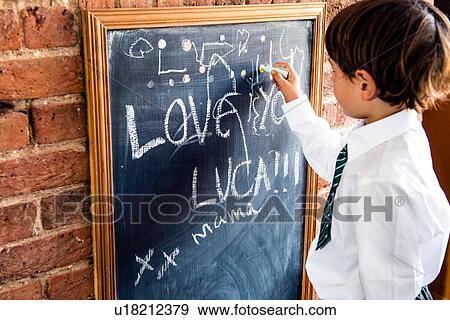 Boy in school uniform writing on blackboard at home View Large Photo Image Stock Photo - Boy in school uniform writing on blackboard at home. Fotosearch