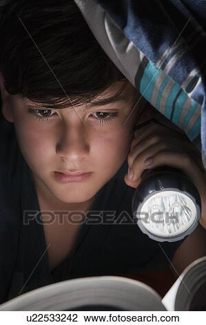 Stock Image - Boy reading with torch under blanket. Fotosearch
