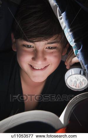 Stock Photo - Boy reading with torch under blanket. Fotosearch