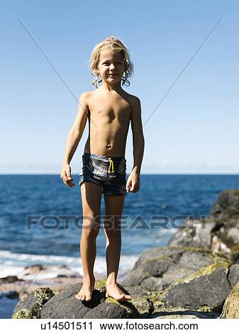 Stock Image - Boy standing on rocks at beach. Fotosearch