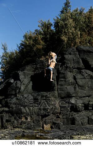Stock Image - Boys climbing cliff in swimwear. Fotosearch
